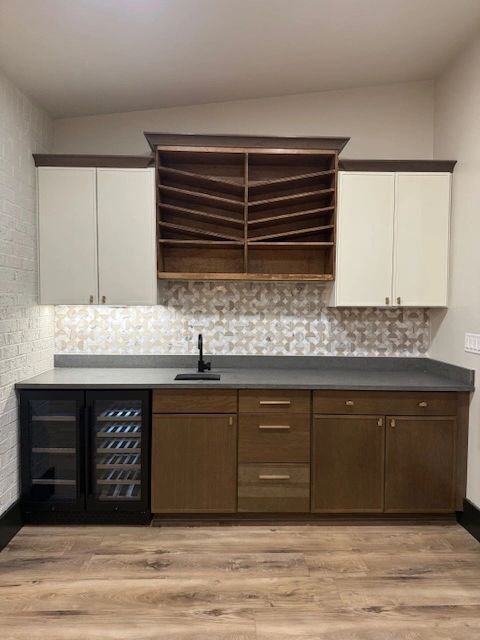 Custom wet bar with wood cabinetry, wine storage, a beverage refrigerator and patterned backsplash