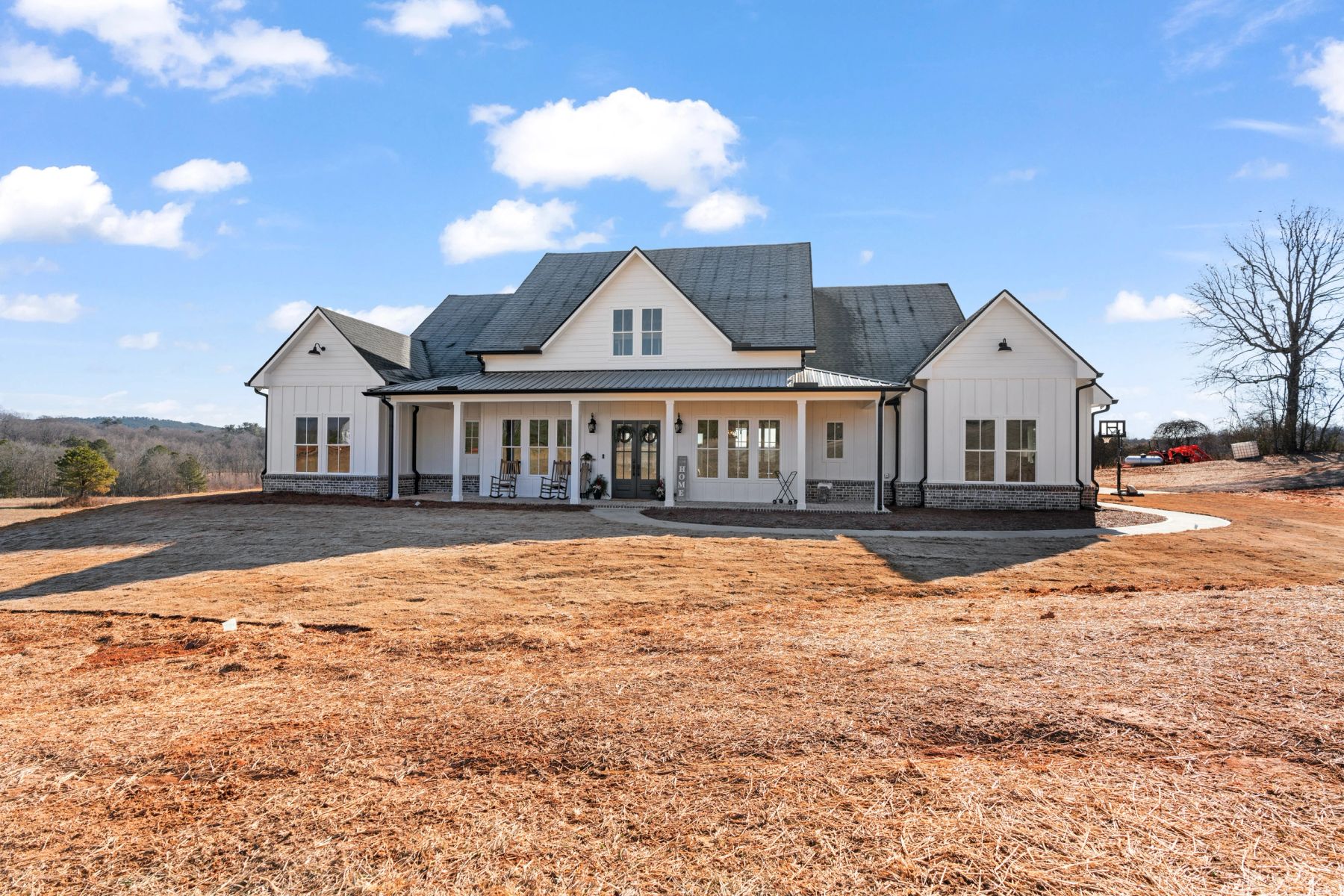 Custom white farmhouse with a broad front porch, multiple gables and black-framed entry doors